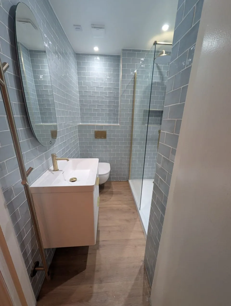 Blue-tiled shower room with vanity storage and illuminated mirror