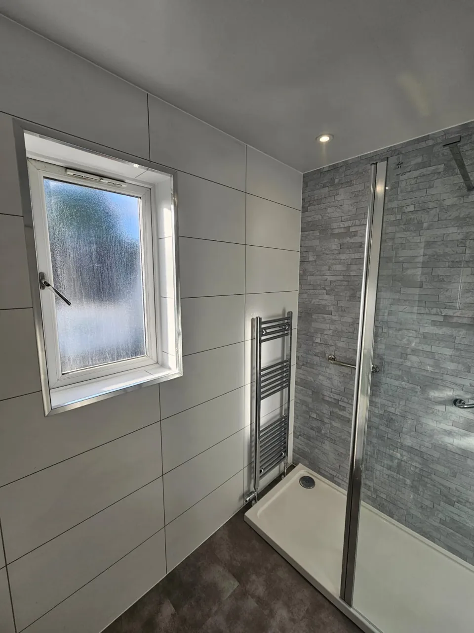 Glass shower enclosure with grey walls and chrome fittings