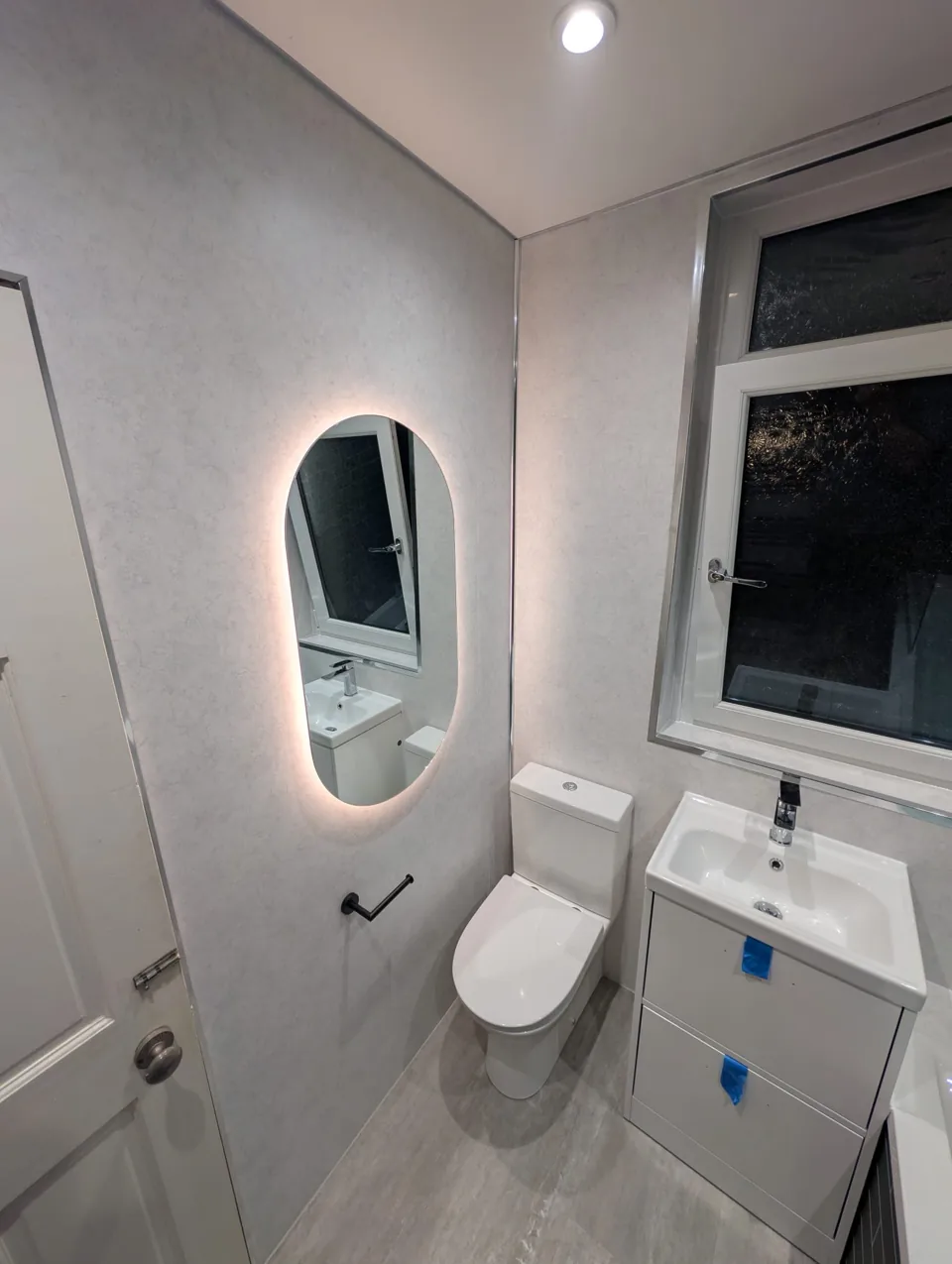 White vanity and toilet beneath an illuminated mirror